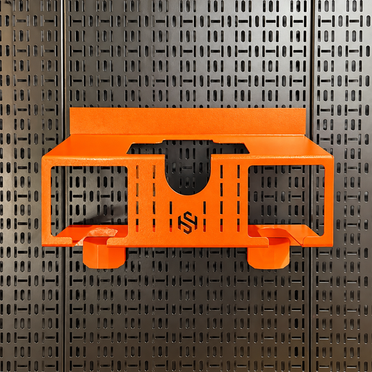 Bright orange metal wall-mounted shelf or organizer bracket with a black stylized logo in the center, shown against a dark perforated pegboard background.