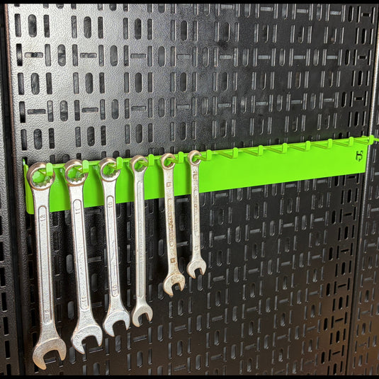 Set of wrenches on a green holder against a black pegboard background