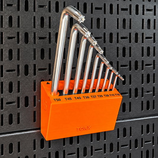A set of silver metal lock picks in graduated sizes stored in a bright orange plastic holder, mounted on a black perforated metal board. The brand name 'TORX' is visible on the holder.
