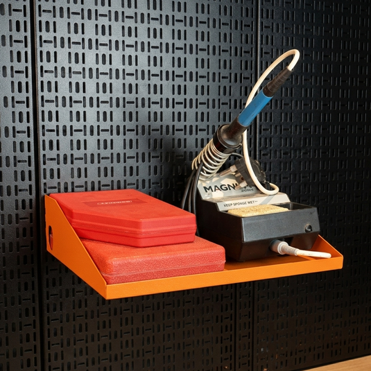 Orange shelf with red blocks and a black and orange tool against a black patterned wall.